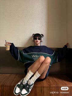 Person in an oversized sweatshirt, sunglasses, and headphones sitting indoors