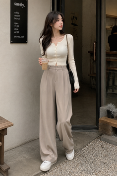 Woman in a cropped cardigan and wide leg pants holding a drink outside a cafe