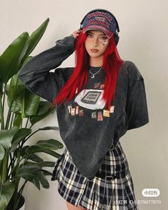 Woman with long red hair wearing a plaid skirt and oversized shirt indoors