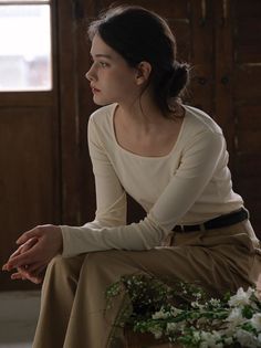 Woman with dark hair in a long sleeve shirt and khaki pants, sitting indoors