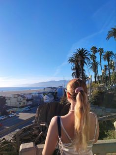 Woman with a ponytail looking out at a beach and cityscape with palm trees