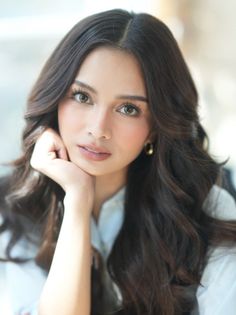 Woman with long wavy hair and light blue shirt, resting chin on hand