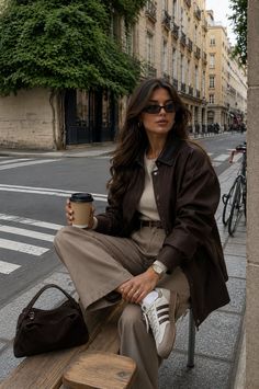 Woman with long hair and sunglasses sitting on a bench on a city street