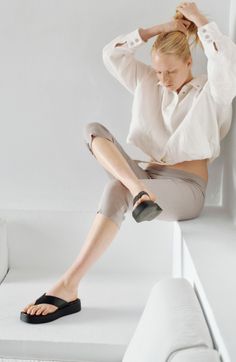 Woman with blonde hair in a white shirt and ribbed pants sitting indoors