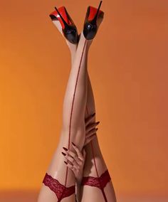 Woman's legs in red lace stockings and high heels against an orange background