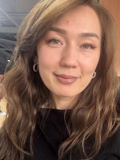Woman with long wavy hair and hoop earrings smiling at the camera