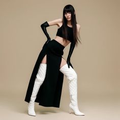 Woman with long black hair in a crop top, long skirt, and thigh-high boots