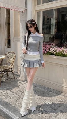 Woman in an off-shoulder top and pleated skirt with leg warmers outdoors