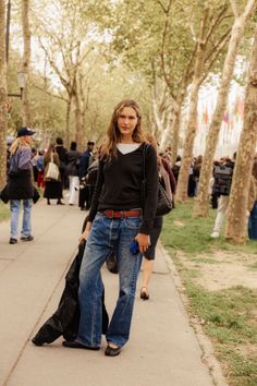 Woman with long hair wearing blue jeans and a black sweater on a tree-lined street
