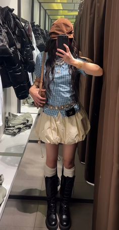 Person in a plaid shirt, bubble skirt, and knee-high boots taking a mirror selfie