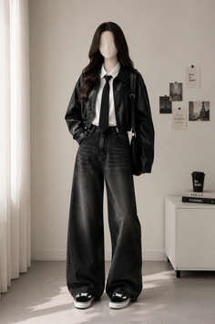 Person with long hair wearing a black leather jacket and wide leg jeans indoors