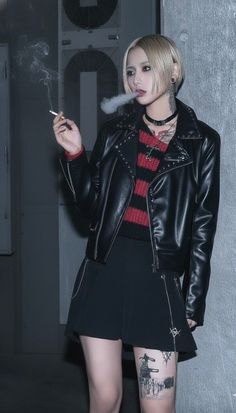 Person with blonde short hair and dark makeup wearing a leather jacket and smoking