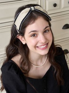 Smiling woman with a headband and pearl jewelry looking up at the camera