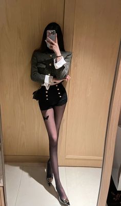 Woman in a cropped jacket and black shorts taking a mirror selfie