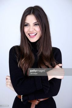 Woman with long dark hair in a black turtleneck and brown belt, smiling with tongue out