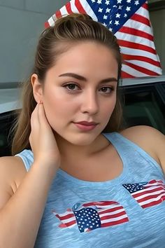 Woman in a blue tank top with an American flag design, posing with her hand on her neck