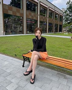 Woman in an orange skirt and black top sitting on a park bench