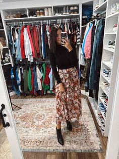 Woman in a black turtleneck and floral skirt taking a mirror selfie in a walk-in closet