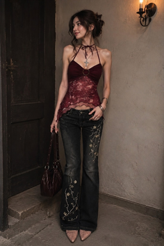 Woman in a red halter top and embroidered jeans holding a handbag indoors