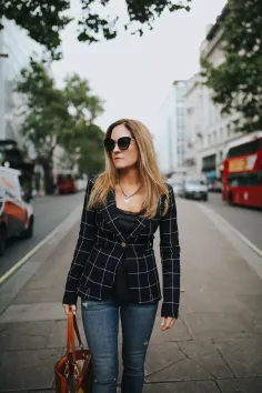 Woman in a plaid blazer and jeans walking on a city street