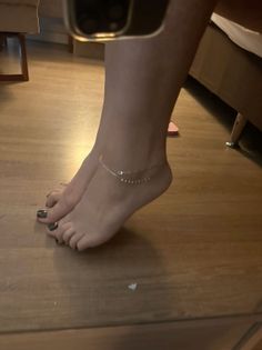 Feet with an anklet and dark nail polish on a wooden floor