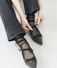 Person tying black lace-up sheer socks over ballet flats with black jeans