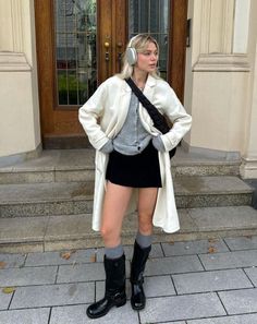 Blonde woman in a white coat, black mini skirt, and boots with headphones outdoors