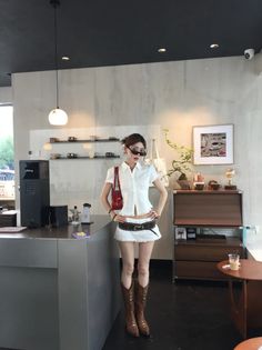 Woman in a white crop top and mini skirt with cowboy boots and sunglasses indoors
