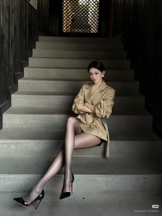 Woman in a trench coat and black pantyhose sitting on stairs indoors