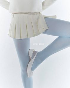 Person wearing a pleated skirt, blue tights, and white shoes in a studio