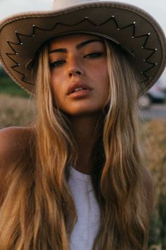 Woman with long blonde hair wearing a cowboy hat outdoors at golden hour