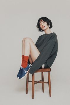 Woman with short hair wearing an oversized sweatshirt, red socks, and blue sneakers