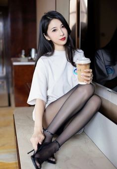 Woman in a white t-shirt and black pantyhose holding a coffee cup indoors