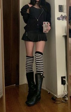 Person in a black hoodie, pleated skirt, and striped knee-high socks taking a mirror selfie