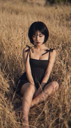 Woman in a black dress sitting in dry grass with soft lighting