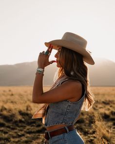 Woman in a cowboy hat and denim vest in a field at golden hour
