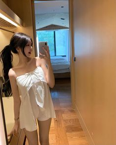 Woman in a white strapless top taking a mirror selfie indoors