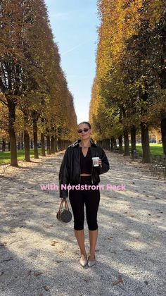 Woman in a black jacket and capri pants walking on a tree-lined path