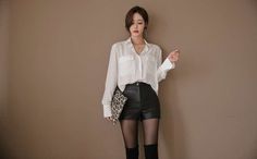 Woman in a white shirt and leather shorts holding a leopard print clutch
