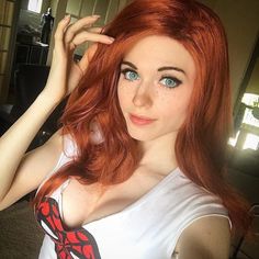 Woman with red hair and blue eyes wearing a white shirt with a spider logo