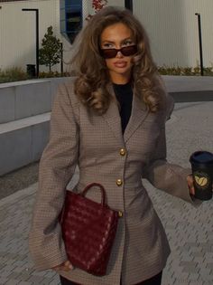 Woman with long wavy hair and sunglasses holding a red handbag and coffee cup