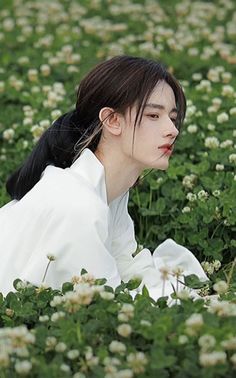 Person with long dark hair in a white shirt sitting in a clover field