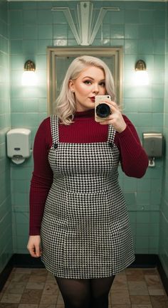 Woman with blonde hair in a houndstooth dress and red turtleneck taking a mirror selfie