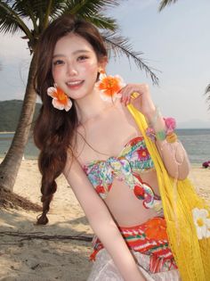 Woman with long hair and flower earrings on a beach, wearing a floral top