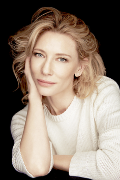 Woman with blonde hair and blue eyes wearing a white sweater against a black background