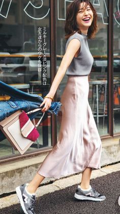 Woman with short hair wearing a pink skirt and grey top, holding a denim jacket and handbag