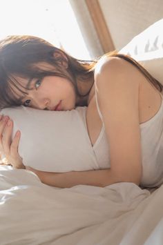 Woman with long hair in a white tank top lying on a bed