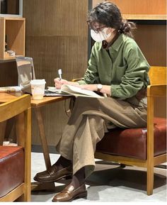 Person wearing glasses and a face mask, working on a laptop and writing in a notebook