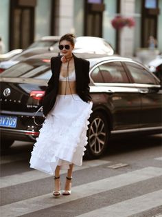 Woman in a white bralette and ruffled skirt with a black blazer on a street