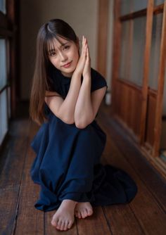 Woman with long hair in a dark dress sitting on a wooden floor indoors